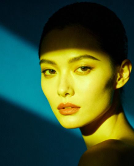 Visage de femme en gros plan, lumière jaune sur fond bleu pétrole